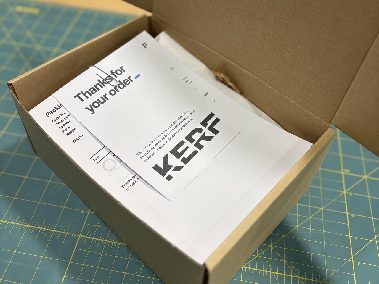 An open KERF box holding a packing slip and a Thanks for your order card, on a cutting mat