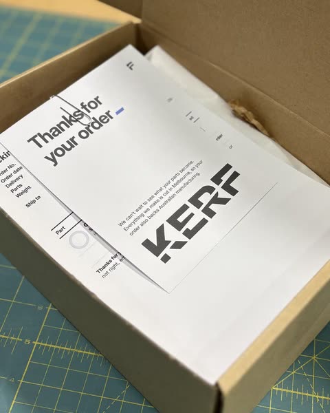 An open cardboard box holding a KERF packing slip and a Thanks for your order card, on a green cutting mat.